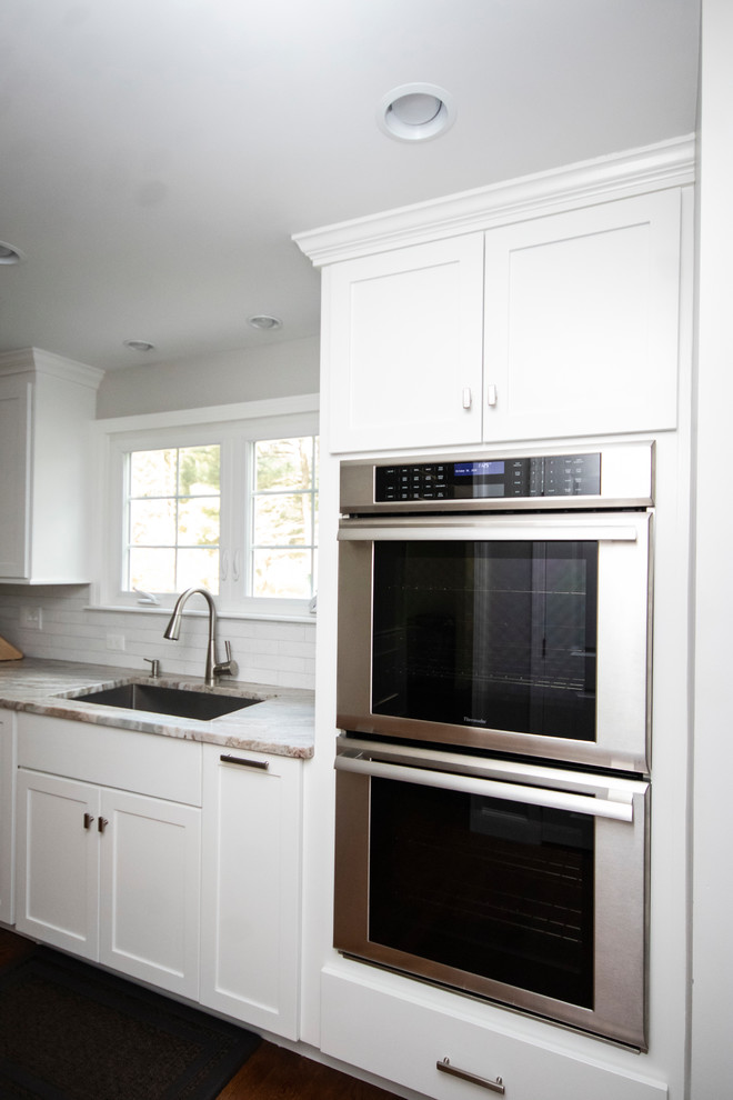 ボストンにある高級な広いトランジショナルスタイルのおしゃれなキッチン (アンダーカウンターシンク、シェーカースタイル扉のキャビネット、白いキャビネット、御影石カウンター、白いキッチンパネル、レンガのキッチンパネル、シルバーの調理設備、濃色無垢フローリング、茶色い床、白いキッチンカウンター) の写真