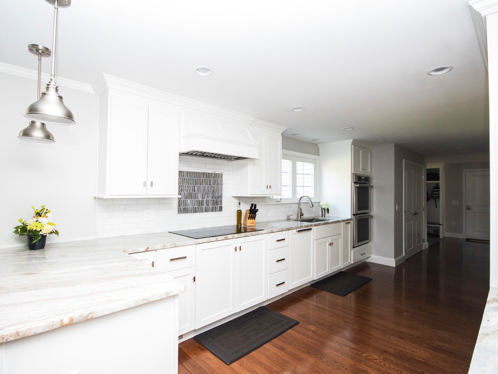ボストンにある高級な広いトランジショナルスタイルのおしゃれなキッチン (アンダーカウンターシンク、シェーカースタイル扉のキャビネット、白いキャビネット、御影石カウンター、白いキッチンパネル、レンガのキッチンパネル、シルバーの調理設備、濃色無垢フローリング、茶色い床、白いキッチンカウンター) の写真