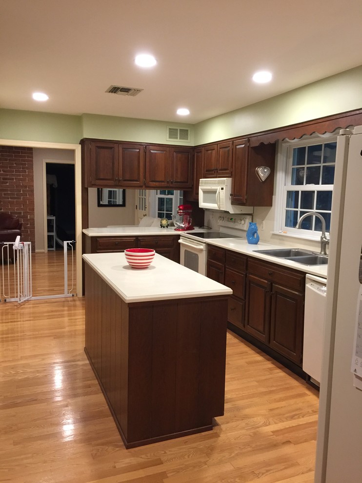 Klassisk inredning av ett mellanstort kök, med en nedsänkt diskho, luckor med upphöjd panel, bruna skåp, bänkskiva i kvartsit, vitt stänkskydd, vita vitvaror, mellanmörkt trägolv, en köksö och gult golv