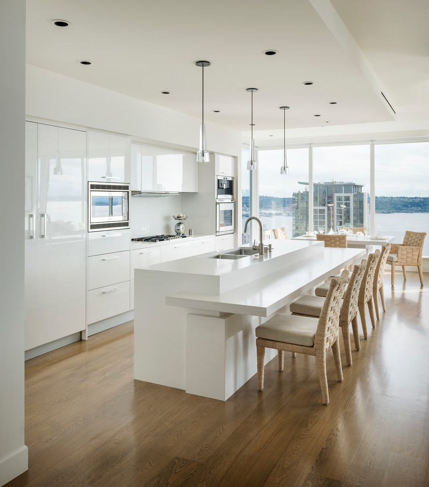 Moderne Küchenbar mit Doppelwaschbecken, flächenbündigen Schrankfronten, weißen Schränken, Küchenrückwand in Weiß, Küchengeräten aus Edelstahl, braunem Holzboden und Kücheninsel in Seattle