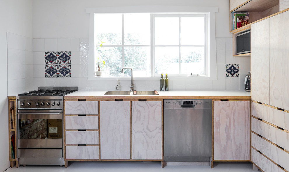 Ejemplo de cocinas en L contemporánea con fregadero encastrado, armarios con rebordes decorativos, puertas de armario de madera clara, salpicadero blanco y electrodomésticos de acero inoxidable