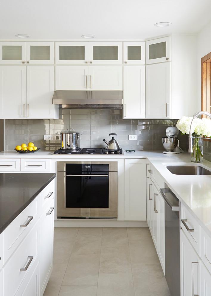 Inredning av ett modernt stort kök, med en undermonterad diskho, luckor med infälld panel, vita skåp, bänkskiva i kvarts, grått stänkskydd, stänkskydd i glaskakel, rostfria vitvaror, klinkergolv i porslin och en köksö
