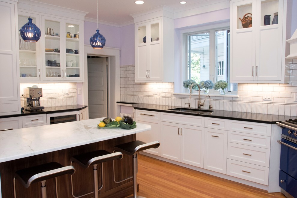 Inspiration for a small transitional l-shaped medium tone wood floor eat-in kitchen remodel in Wilmington with an undermount sink, flat-panel cabinets, white cabinets, granite countertops, white backsplash, ceramic backsplash, paneled appliances and an island