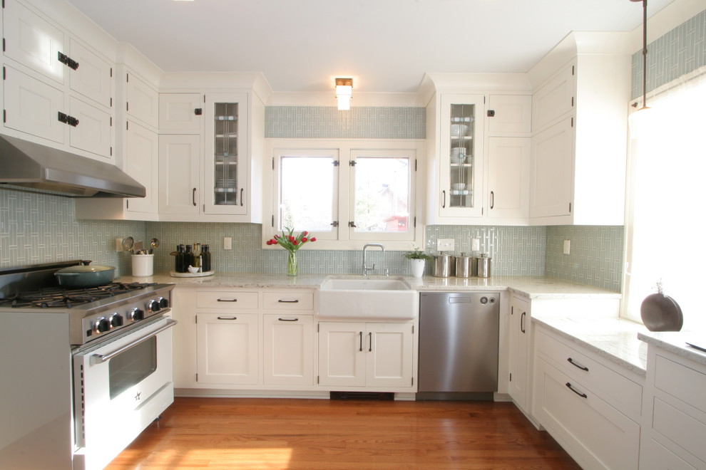 Inredning av ett klassiskt avskilt, mellanstort u-kök, med en rustik diskho, luckor med infälld panel, vita skåp, granitbänkskiva, blått stänkskydd, stänkskydd i glaskakel, rostfria vitvaror och mellanmörkt trägolv