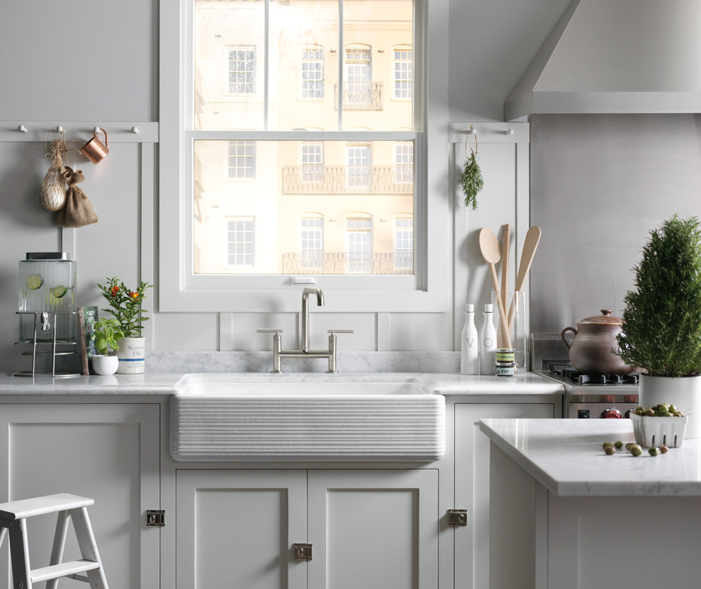 Inredning av ett klassiskt avskilt, mellanstort linjärt kök, med en rustik diskho, skåp i shakerstil, vita skåp, marmorbänkskiva, vitt stänkskydd, fönster som stänkskydd och rostfria vitvaror