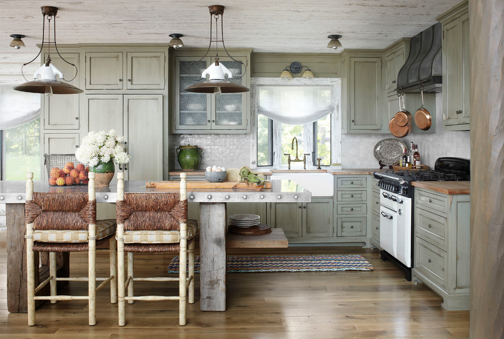 Example of a mountain style l-shaped kitchen design in Milwaukee with a farmhouse sink, shaker cabinets, distressed cabinets, wood countertops, gray backsplash, mosaic tile backsplash and paneled appliances
