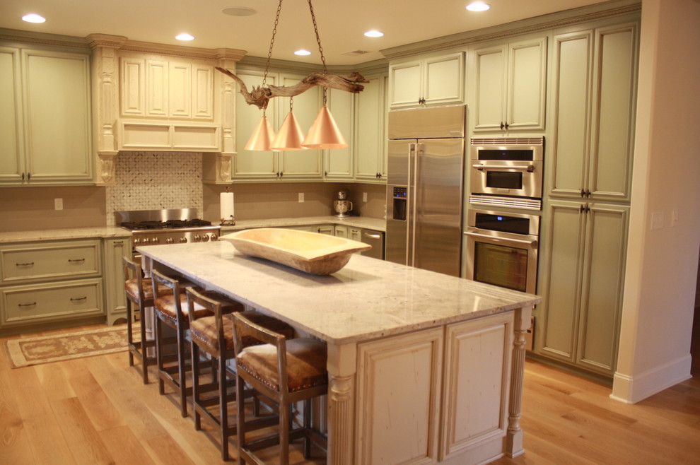 Rustik inredning av ett stort kök, med en rustik diskho, luckor med upphöjd panel, gröna skåp, granitbänkskiva, grått stänkskydd, stänkskydd i keramik, rostfria vitvaror, ljust trägolv och en köksö