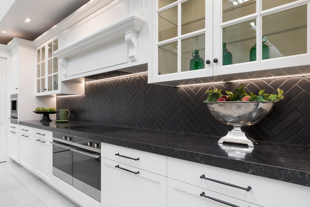 Expansive traditional kitchen/diner in Auckland with a double-bowl sink, shaker cabinets, white cabinets, engineered stone countertops, black splashback, metro tiled splashback, stainless steel appliances, porcelain flooring, an island, grey floors and black worktops.