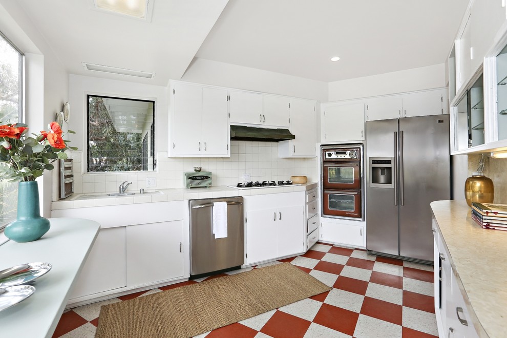 Mid-Century Küche ohne Insel in L-Form mit flächenbündigen Schrankfronten, weißen Schränken, Küchenrückwand in Weiß und Küchengeräten aus Edelstahl in Los Angeles