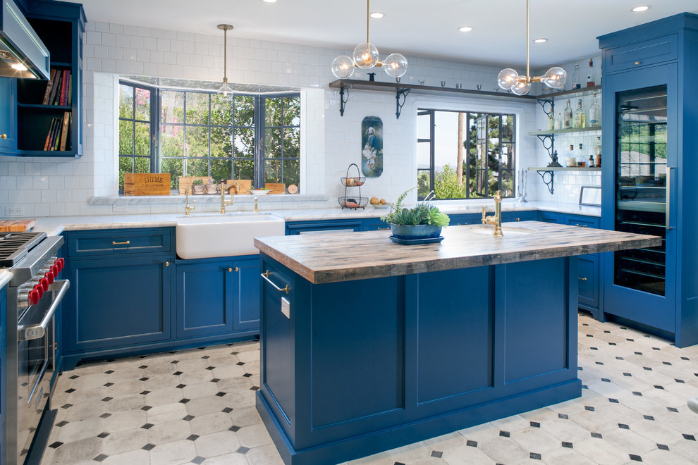 Foto på ett stort medelhavsstil u-kök, med en rustik diskho, luckor med infälld panel, blå skåp, marmorbänkskiva, vitt stänkskydd, stänkskydd i tunnelbanekakel, integrerade vitvaror, betonggolv, en köksö och flerfärgat golv