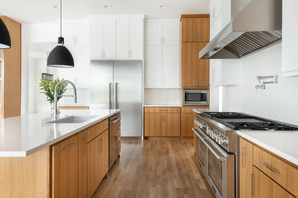 Foto de cocinas en L contemporánea grande abierta con fregadero bajoencimera, armarios con paneles lisos, puertas de armario de madera oscura, encimera de cuarzo compacto, salpicadero blanco, salpicadero de azulejos de cerámica, electrodomésticos de acero inoxidable, suelo de madera en tonos medios, una isla, encimeras blancas y suelo marrón