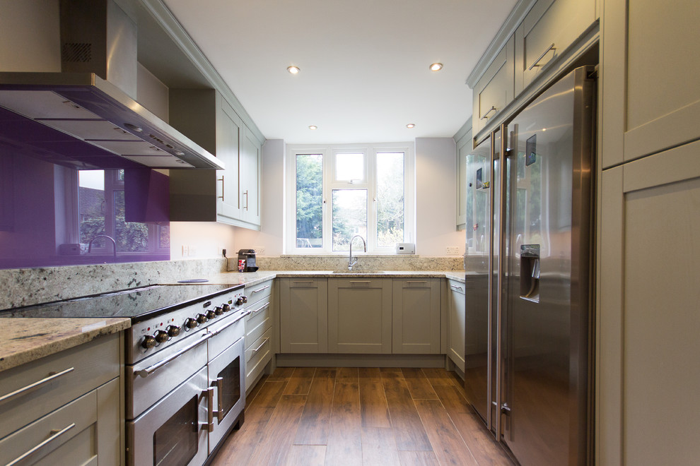 Design ideas for a medium sized modern u-shaped enclosed kitchen in London with an integrated sink, shaker cabinets, grey cabinets, granite worktops, pink splashback, glass sheet splashback, stainless steel appliances, porcelain flooring and no island.