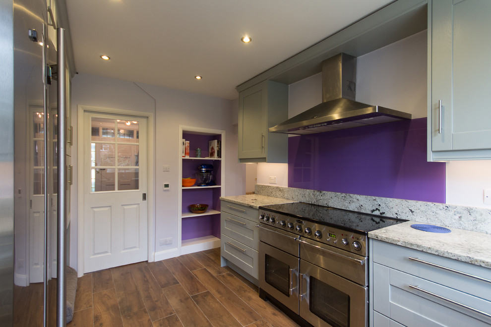 Photo of a medium sized modern u-shaped enclosed kitchen in London with an integrated sink, shaker cabinets, grey cabinets, granite worktops, pink splashback, glass sheet splashback, stainless steel appliances, porcelain flooring and no island.