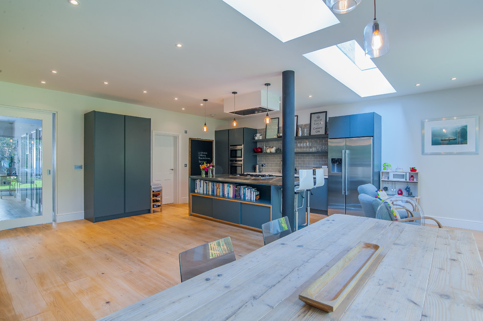 Inspiration for a medium sized contemporary open plan kitchen in Surrey with an integrated sink, flat-panel cabinets, grey cabinets, stainless steel worktops, grey splashback, porcelain splashback, stainless steel appliances, medium hardwood flooring and an island.