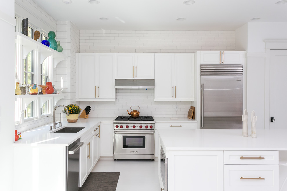 Inredning av ett modernt vit vitt l-kök, med en undermonterad diskho, skåp i shakerstil, vita skåp, vitt stänkskydd, rostfria vitvaror, en köksö och vitt golv
