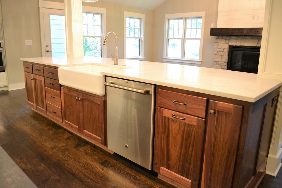 Medium sized country l-shaped open plan kitchen in Kansas City with a belfast sink, shaker cabinets, white cabinets, engineered stone countertops, white splashback, metro tiled splashback, stainless steel appliances, dark hardwood flooring, an island and brown floors.