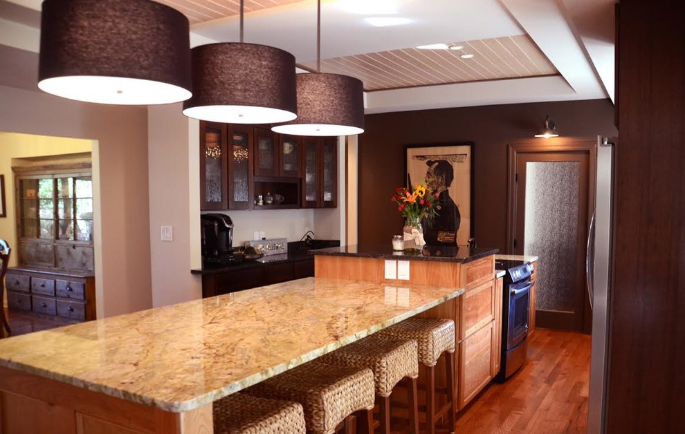 Immagine di una cucina design di medie dimensioni con ante di vetro, top in granito, elettrodomestici in acciaio inossidabile, pavimento in legno massello medio, ante in legno bruno e lavello sottopiano
