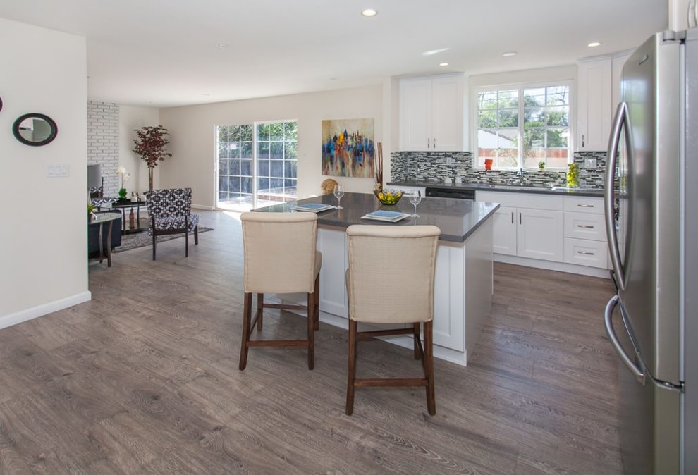 Medium sized traditional u-shaped enclosed kitchen in Los Angeles with shaker cabinets, white cabinets, composite countertops, stainless steel appliances, dark hardwood flooring, an island and green floors.