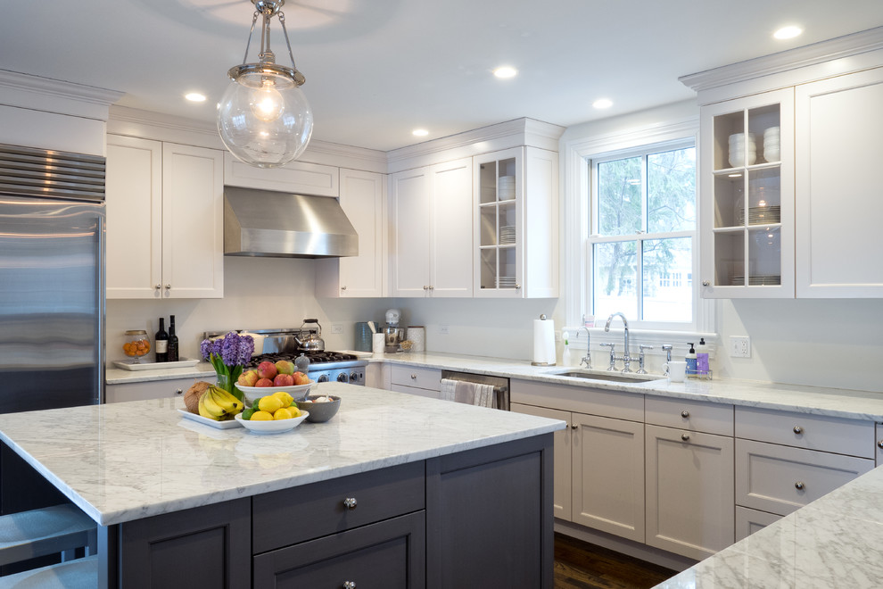 Design ideas for a traditional u-shaped kitchen in Philadelphia with shaker cabinets, white cabinets, white splashback, stainless steel appliances, medium hardwood flooring, an island, brown floors and white worktops.
