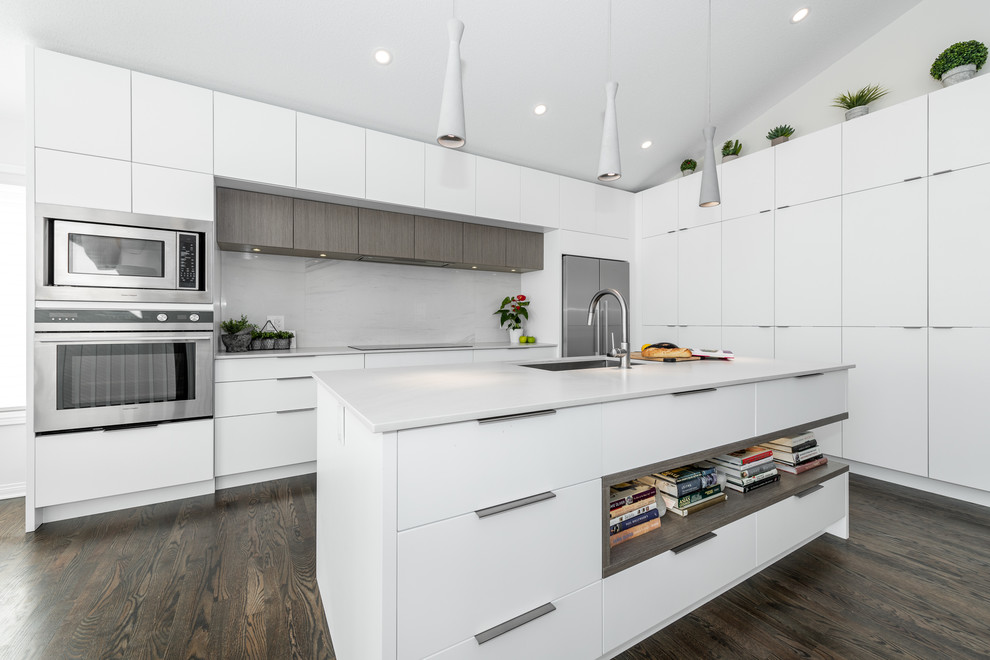 Foto på ett mellanstort funkis grå kök, med en undermonterad diskho, släta luckor, vita skåp, rostfria vitvaror, en köksö, brunt golv, bänkskiva i kvarts, vitt stänkskydd, stänkskydd i porslinskakel och mörkt trägolv