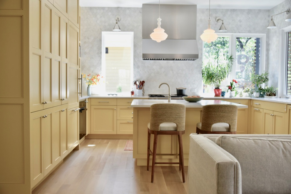 Exempel på ett stort klassiskt vit vitt kök, med en undermonterad diskho, luckor med profilerade fronter, gula skåp, bänkskiva i kvarts, grått stänkskydd, stänkskydd i marmor, svarta vitvaror, mellanmörkt trägolv, en köksö och beiget golv