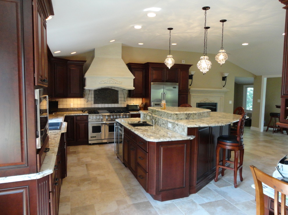 This is an example of a large classic l-shaped kitchen/diner in Chicago with raised-panel cabinets, dark wood cabinets, granite worktops, beige splashback, ceramic splashback, stainless steel appliances, travertine flooring, an island, a double-bowl sink and beige floors.