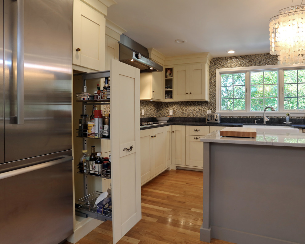 Example of a large classic l-shaped light wood floor enclosed kitchen design in Boston with a farmhouse sink, shaker cabinets, beige cabinets, stainless steel appliances and an island