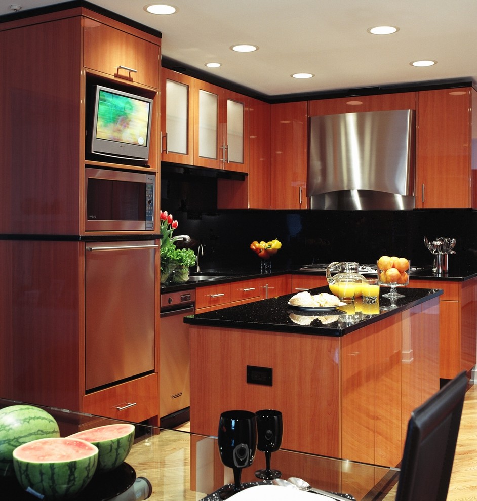 Immagine di una cucina minimal di medie dimensioni con ante lisce, ante in legno scuro, paraspruzzi nero, elettrodomestici in acciaio inossidabile, lavello sottopiano, top in granito e parquet chiaro
