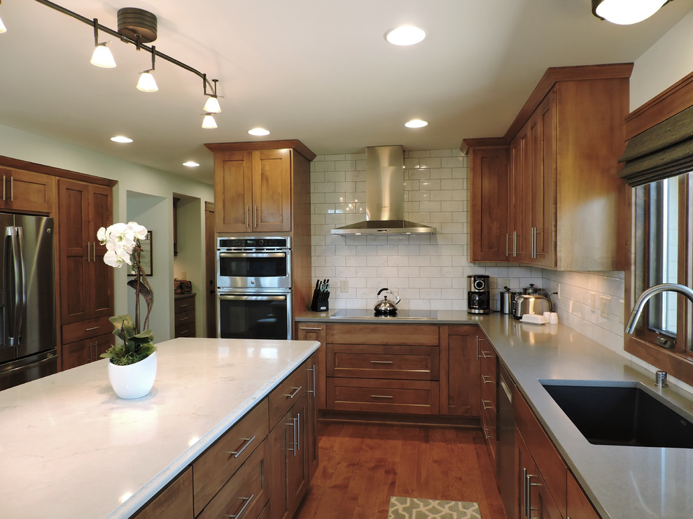 Mid-sized transitional l-shaped medium tone wood floor and brown floor eat-in kitchen photo in Milwaukee with an undermount sink, recessed-panel cabinets, brown cabinets, marble countertops, white backsplash, subway tile backsplash, stainless steel appliances and an island