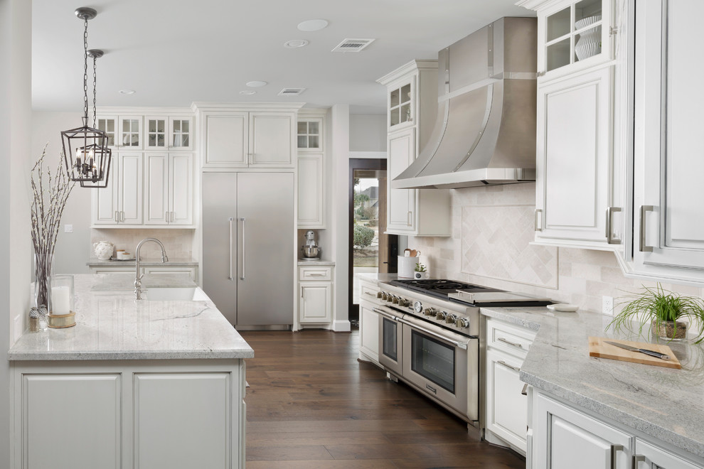Klassisk inredning av ett stort vit vitt l-kök, med en rustik diskho, luckor med upphöjd panel, vita skåp, granitbänkskiva, vitt stänkskydd, stänkskydd i travertin, rostfria vitvaror, mörkt trägolv, en köksö och brunt golv