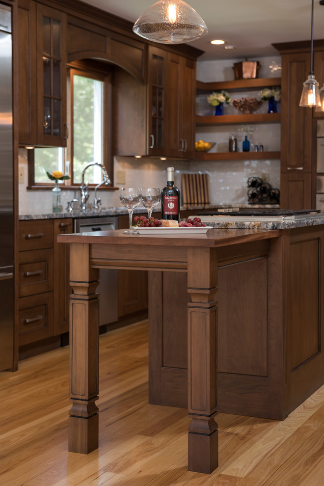 Klassisk inredning av ett mellanstort kök, med en enkel diskho, luckor med infälld panel, skåp i mellenmörkt trä, granitbänkskiva, vitt stänkskydd, stänkskydd i glaskakel, rostfria vitvaror, mellanmörkt trägolv och en köksö