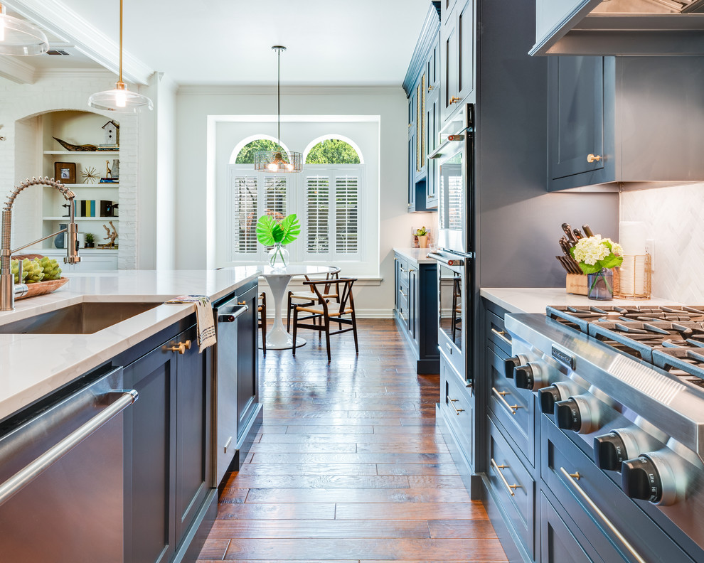 Example of a large transitional l-shaped medium tone wood floor and brown floor open concept kitchen design in Dallas with an undermount sink, shaker cabinets, blue cabinets, marble countertops, gray backsplash, marble backsplash, stainless steel appliances, an island and white countertops