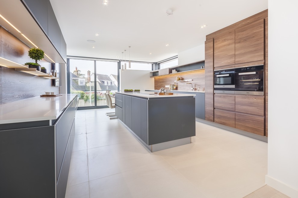 Zweizeilige Moderne Küche mit flächenbündigen Schrankfronten, grauen Schränken, schwarzen Elektrogeräten, Kücheninsel, beigem Boden und weißer Arbeitsplatte in Dorset