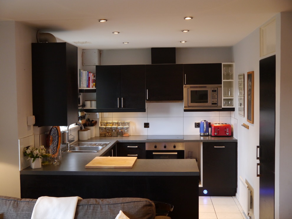 Medium sized contemporary u-shaped open plan kitchen in London with a double-bowl sink, flat-panel cabinets, black cabinets, laminate countertops, white splashback, ceramic splashback, stainless steel appliances, ceramic flooring and a breakfast bar.