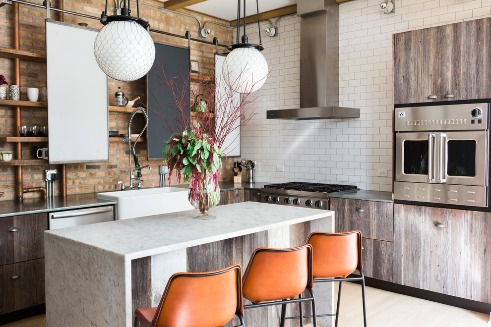 Urban l-shaped kitchen in Chicago with a belfast sink, marble worktops, white splashback, metro tiled splashback, stainless steel appliances, light hardwood flooring, an island, beige floors, white worktops, flat-panel cabinets and distressed cabinets.