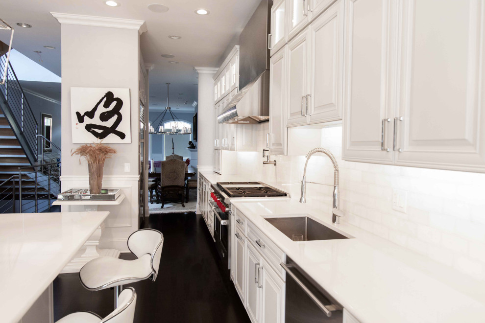 Photo of a contemporary kitchen in Chicago with a submerged sink, raised-panel cabinets, white cabinets, white splashback, stainless steel appliances, dark hardwood flooring, an island and white worktops.