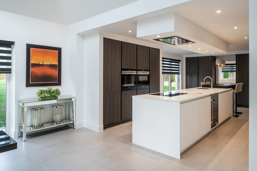 This is an example of a contemporary l-shaped kitchen/diner in Kent with a submerged sink, flat-panel cabinets, black appliances, an island, beige floors, white worktops and dark wood cabinets.