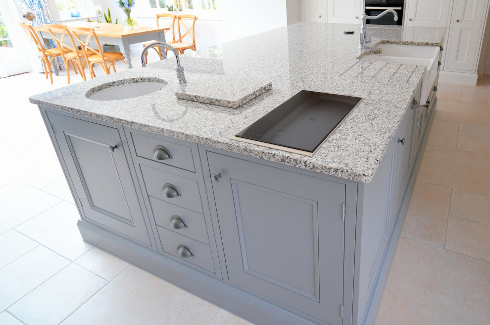 Photo of a large rural kitchen/diner in Essex with a belfast sink, beaded cabinets, grey cabinets, granite worktops, black appliances, ceramic flooring, an island, beige floors and multicoloured worktops.