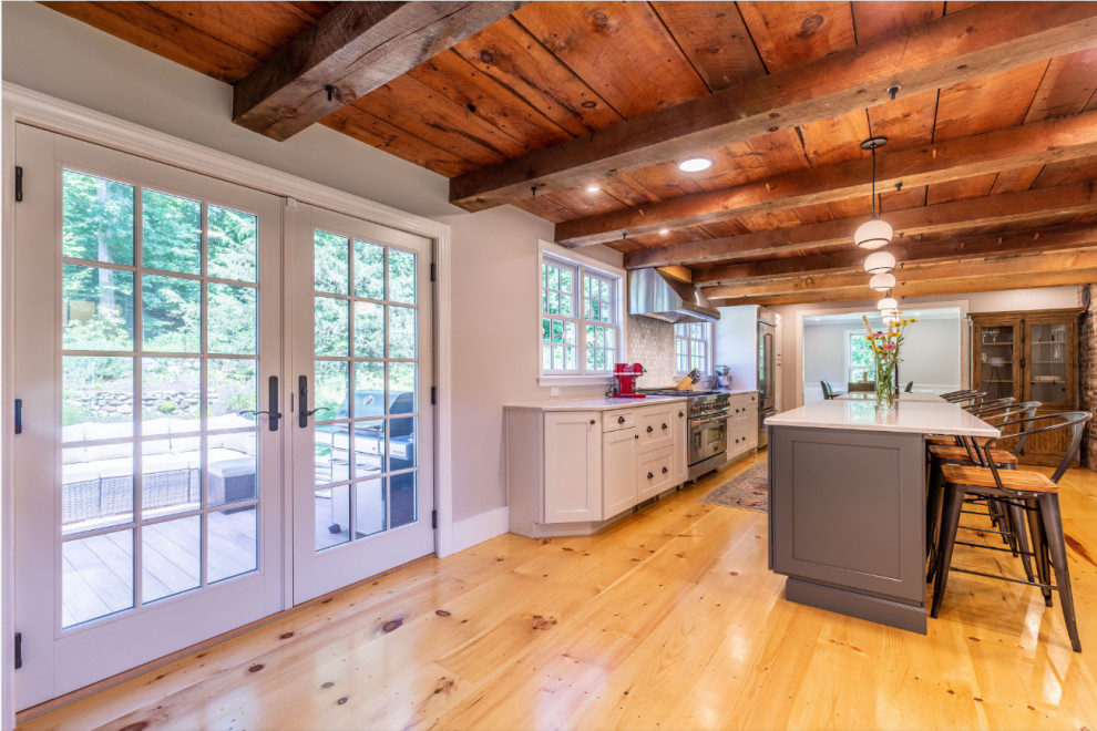 Foto di una cucina parallela country con paraspruzzi bianco, pavimento in legno massello medio, 2 o più isole, top bianco e soffitto in legno