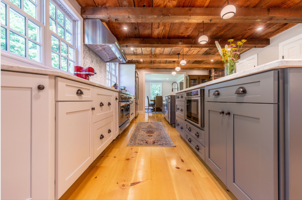 Zweizeilige Landhausstil Küche mit Küchenrückwand in Weiß, braunem Holzboden, zwei Kücheninseln, weißer Arbeitsplatte, Küchengeräten aus Edelstahl und Holzdecke in Boston