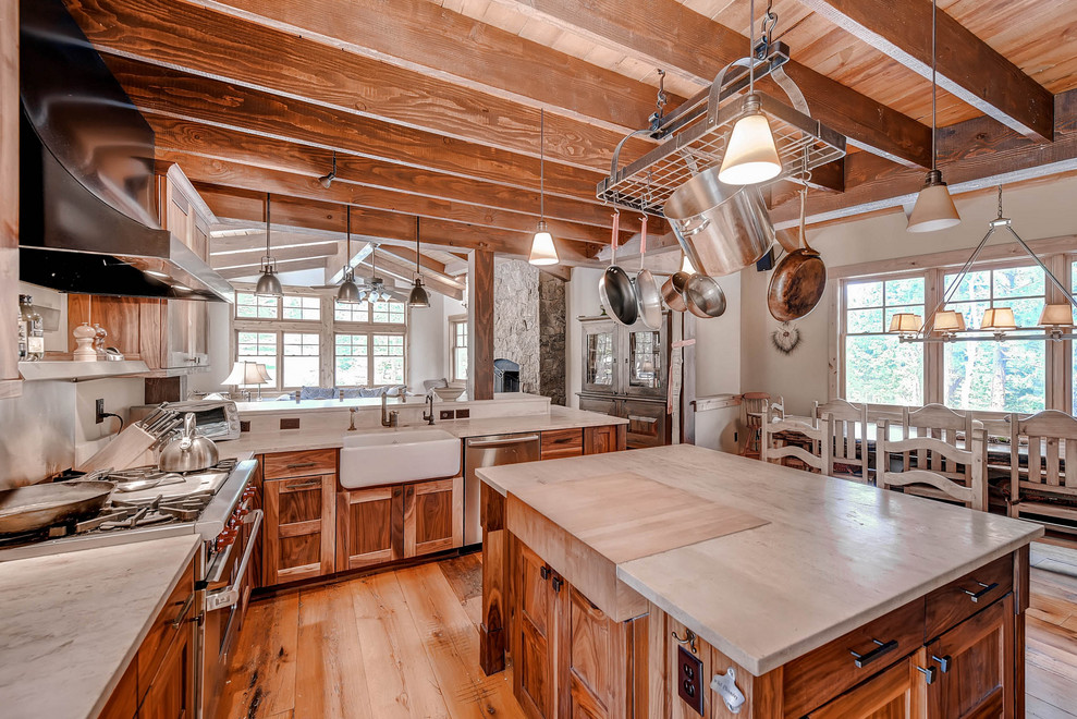 Open concept kitchen - rustic light wood floor and exposed beam open concept kitchen idea in Denver with recessed-panel cabinets, medium tone wood cabinets, an island, gray countertops, a farmhouse sink and stainless steel appliances