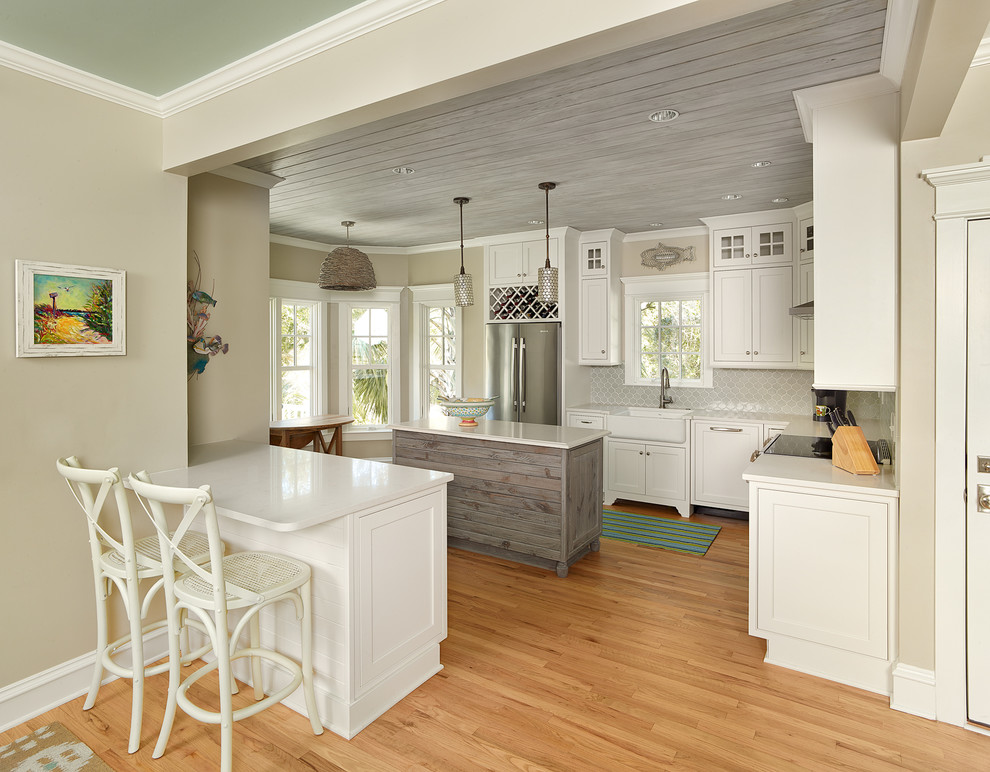 Beach style kitchen in Charleston with a belfast sink, engineered stone countertops, stainless steel appliances, light hardwood flooring and an island.