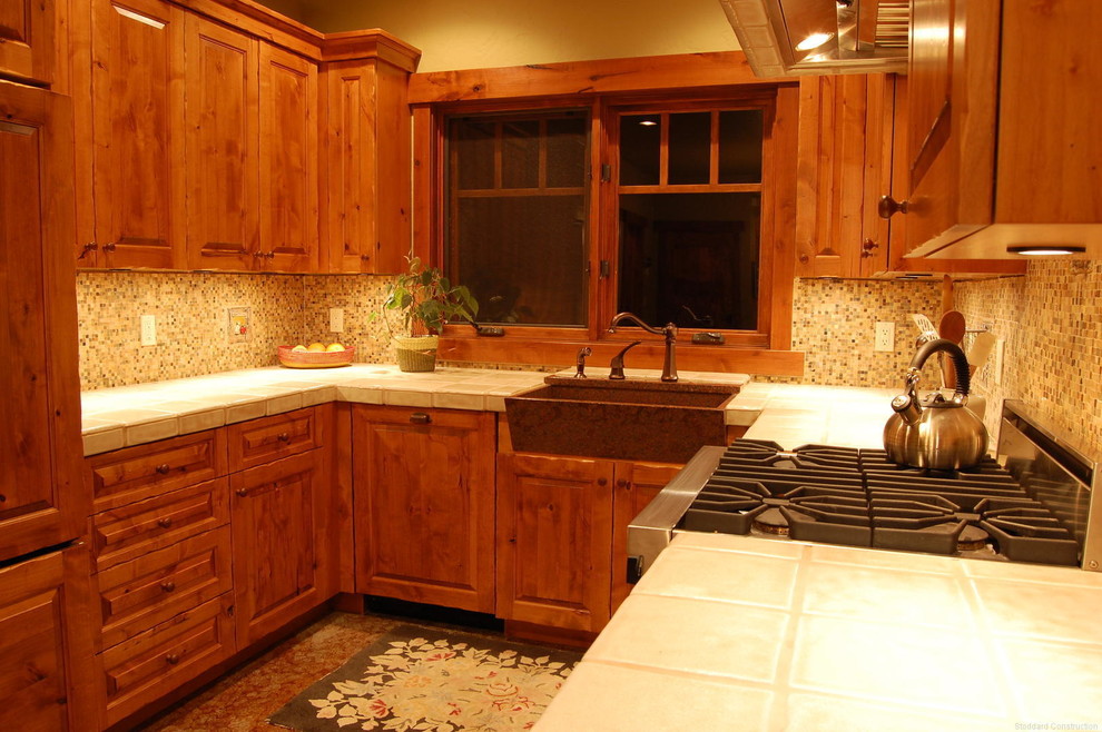 Foto på ett avskilt, mellanstort amerikanskt u-kök, med en rustik diskho, luckor med upphöjd panel, skåp i mellenmörkt trä, rostfria vitvaror, kaklad bänkskiva, beige stänkskydd, stänkskydd i mosaik och brunt golv