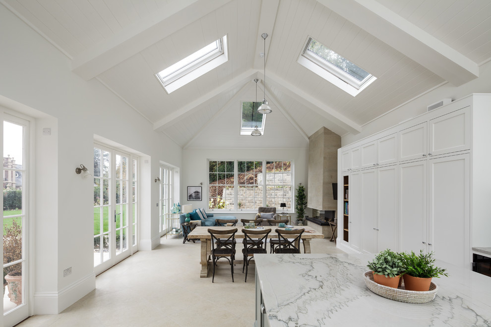 Photo of a large traditional kitchen/diner in Surrey with recessed-panel cabinets, white cabinets, marble worktops, marble splashback, white appliances, an island and beige floors.