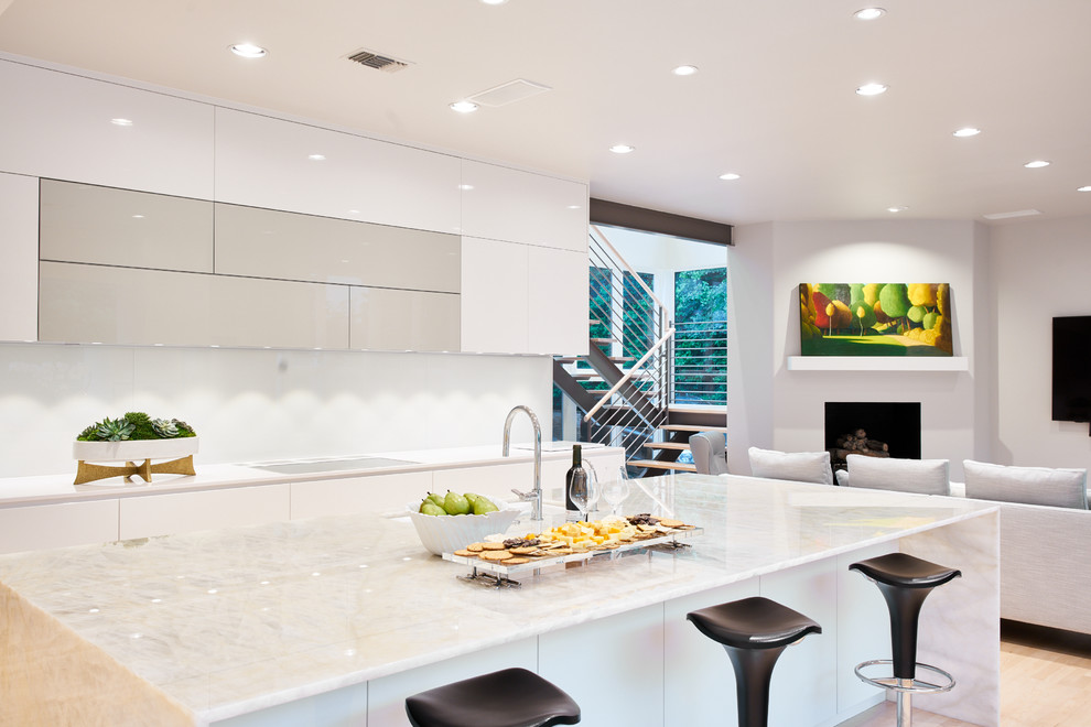 Large contemporary l-shaped kitchen/diner in Dallas with a submerged sink, flat-panel cabinets, white cabinets, engineered stone countertops, white splashback, glass sheet splashback, white appliances, light hardwood flooring, an island, white floors and white worktops.