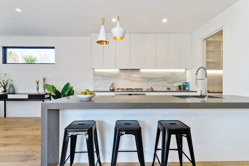 Offene, Zweizeilige, Mittelgroße Moderne Küche mit Unterbauwaschbecken, weißen Schränken, Quarzwerkstein-Arbeitsplatte, Küchengeräten aus Edelstahl, hellem Holzboden, Kücheninsel, braunem Boden und grauer Arbeitsplatte in Melbourne