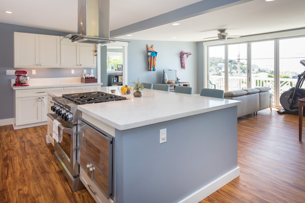Large transitional l-shaped light wood floor open concept kitchen photo in Hawaii with a farmhouse sink, shaker cabinets, white cabinets, quartz countertops, blue backsplash, subway tile backsplash, stainless steel appliances and an island