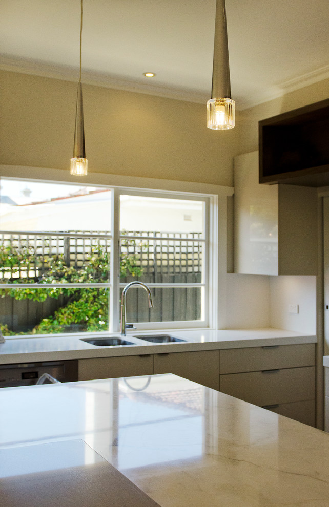This is an example of a medium sized contemporary l-shaped kitchen/diner in Melbourne with a submerged sink, flat-panel cabinets, beige cabinets, engineered stone countertops, beige splashback, stone slab splashback, stainless steel appliances, medium hardwood flooring and an island.