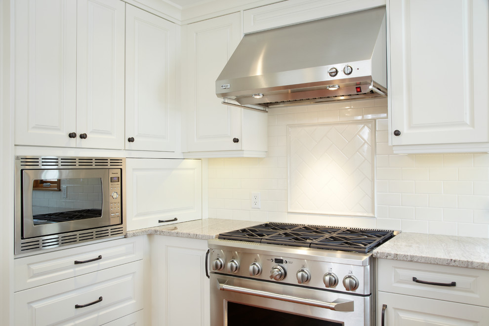 Imagen de cocina tradicional con armarios con paneles con relieve, encimera de granito, salpicadero blanco y una isla