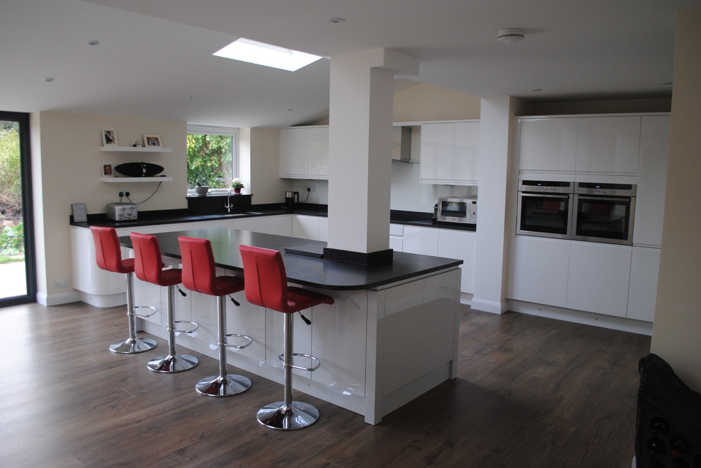 Exempel på ett stort modernt kök med öppen planlösning, med en undermonterad diskho, släta luckor, vita skåp, granitbänkskiva, vitt stänkskydd, glaspanel som stänkskydd, rostfria vitvaror och en köksö